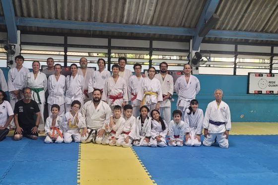 Turma de crianças, jovens e adultos reunida no fim do treino, no ginásio do CEE Cambuci